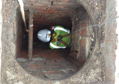 Drain Technology employee is wearing a harness being lowered into a brick drain site.