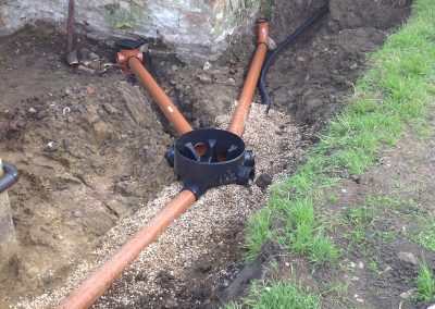 Shows a dug out area between a builing and field where a new drain systwm and pipes have been installed in a Repairs & Excavations job