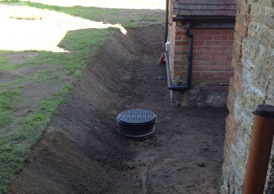 Repairs & Excavations job Around the sides of a brick building a ditch has been built in the field to expose a drain opening