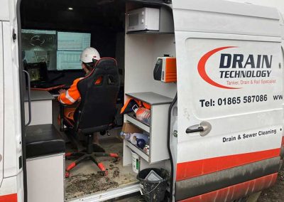 Drain technology van open with employee sat inside analysing 4 large screens and 1 separate screen.