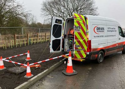 Rear view to the right of a Drain Technology CCTV Site Investigation Uint van open on-site. The van is parked on the side of the road. The back of the van is open with a tape and coned-off area.
