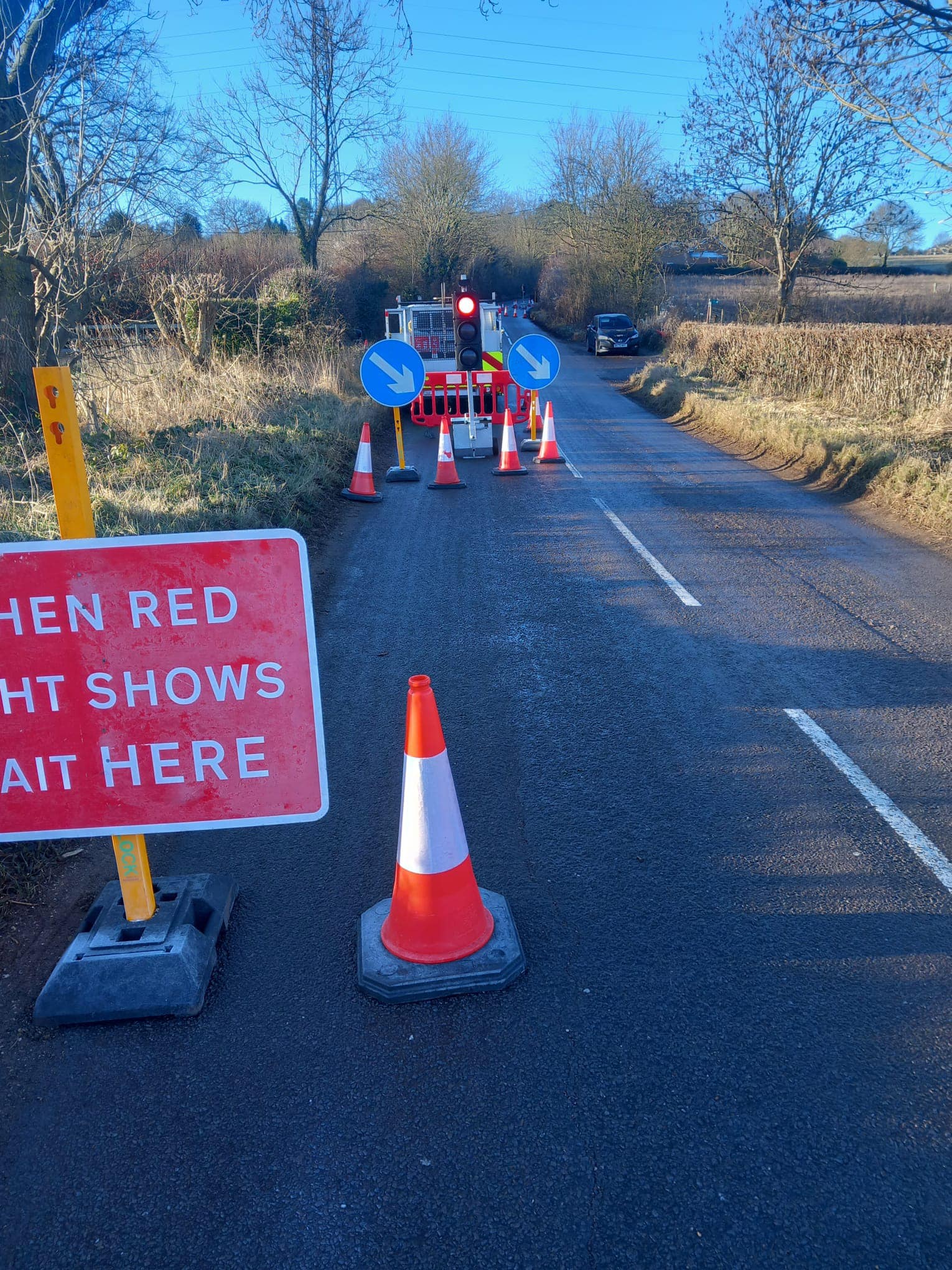Traffic management cones and signs set up on a country-side road for roadworks.