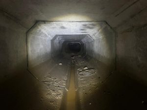 Dark drain tunnel with torch illuminating the path