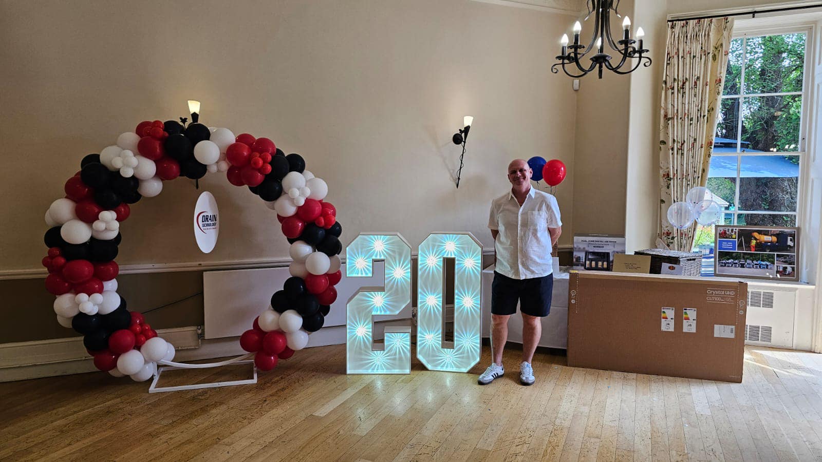 Drain Technology Director in front of balloon and "20" sign for anniversary party.