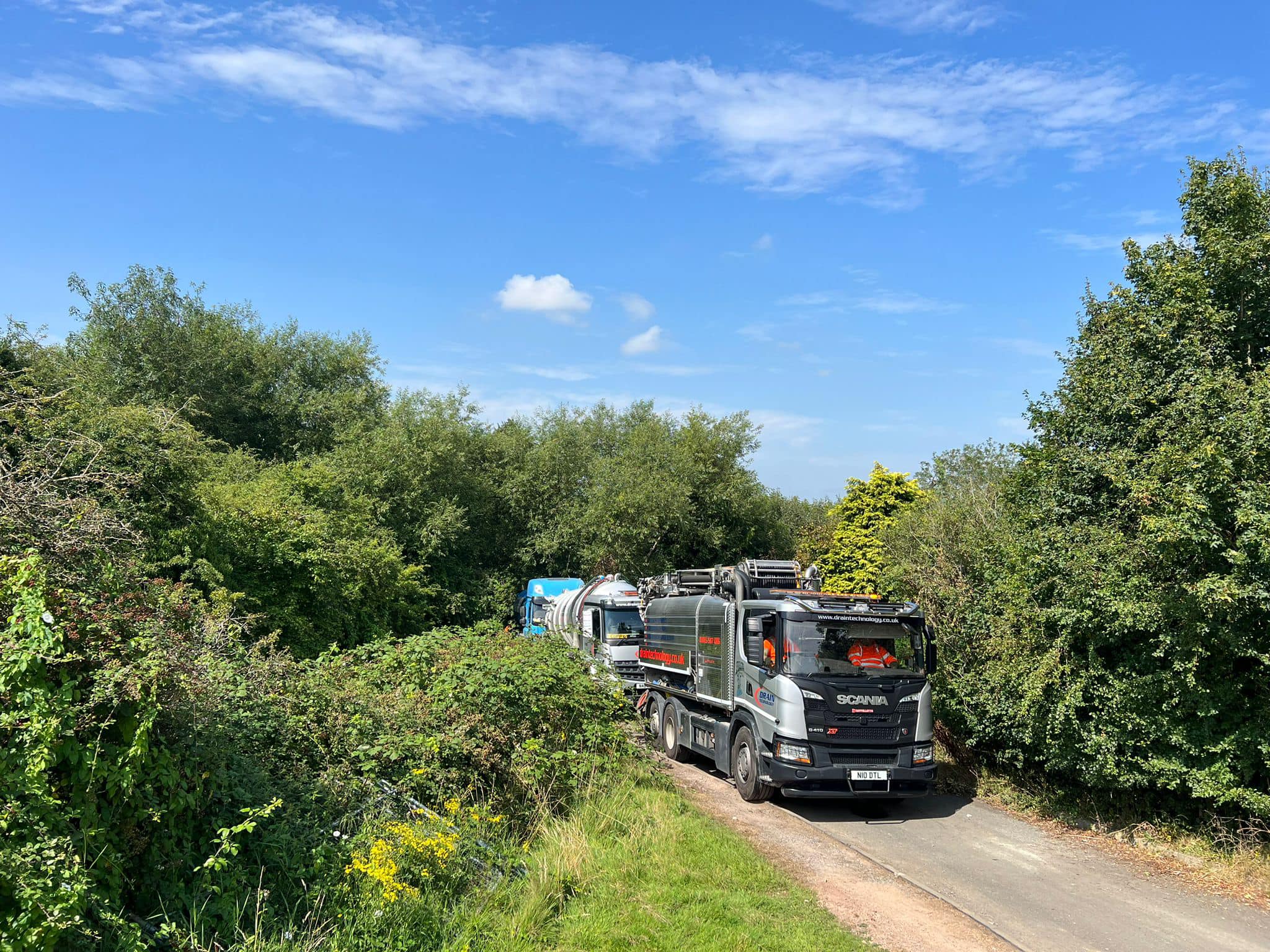 Drain Technology tanker driving with trees either side of the road.