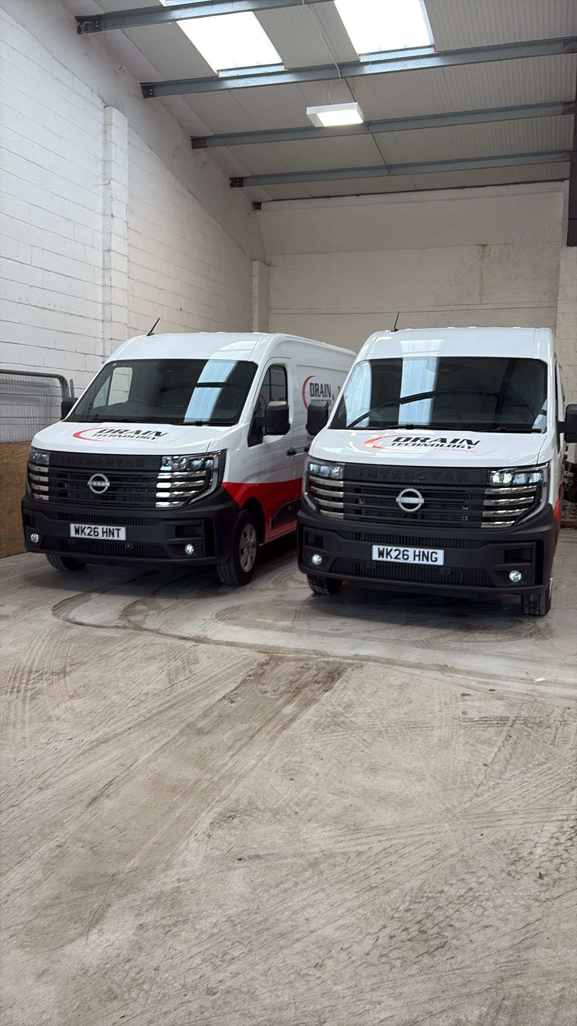 Two Drain Technology vans inside a white warehouse