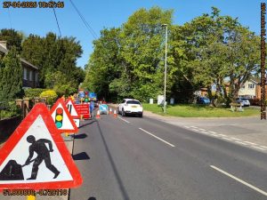 Various traffic signs leading to temporary lights on a road with roadworks. 