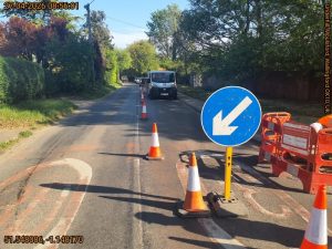 Blue arrow sign pointing towards an open lane on a road. The other side of the road is closed by traffic cones and a TTM van