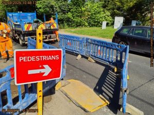 Pedestrians sign leading to a fenced off walkway on a road. 