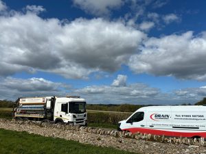 Drain Technology tanker and van in farm field behind a stone wall on a bright day