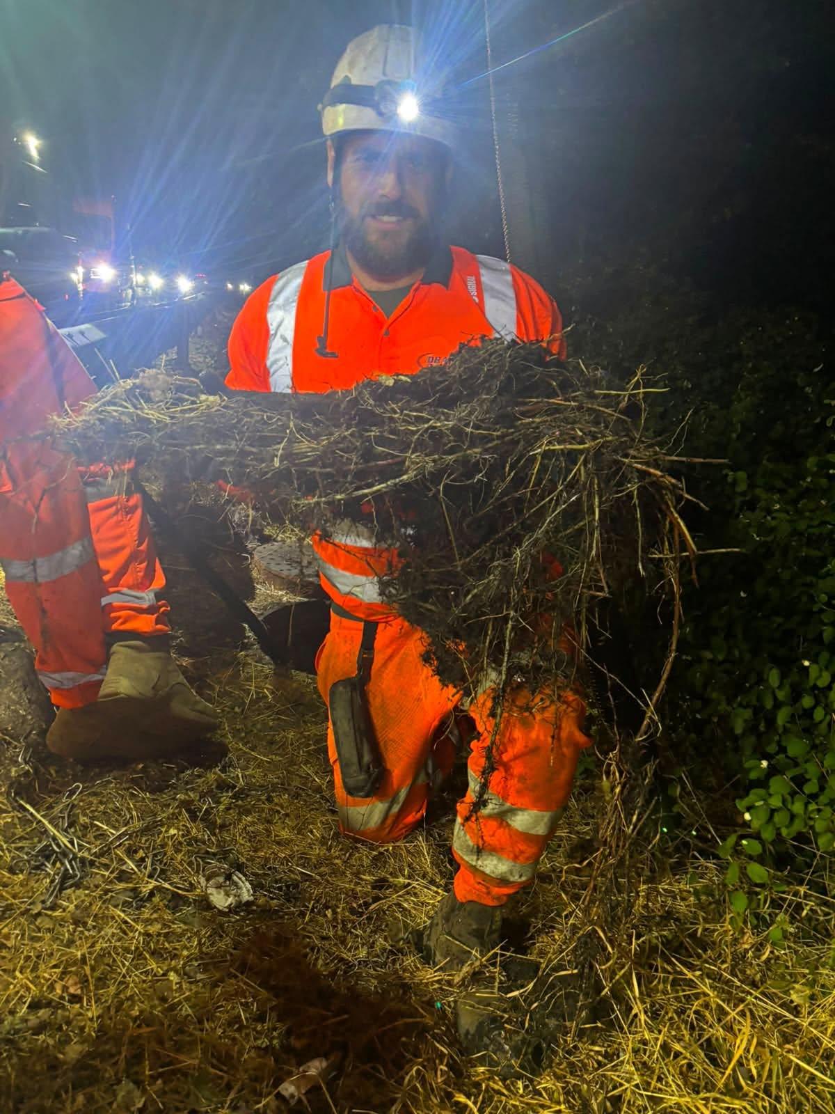 man in overalls at night with a head torch on holding mud and dirt