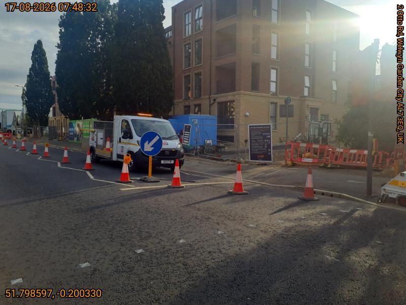 Traffic cones closing a section of road with a van parked in it by a large building
