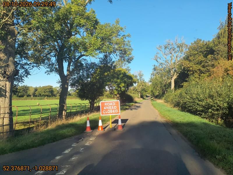 red road closed sign with orange traffic cones and greenery behind