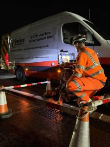 Man in orange hi vis next to Drain Technology van on the side of the road at night